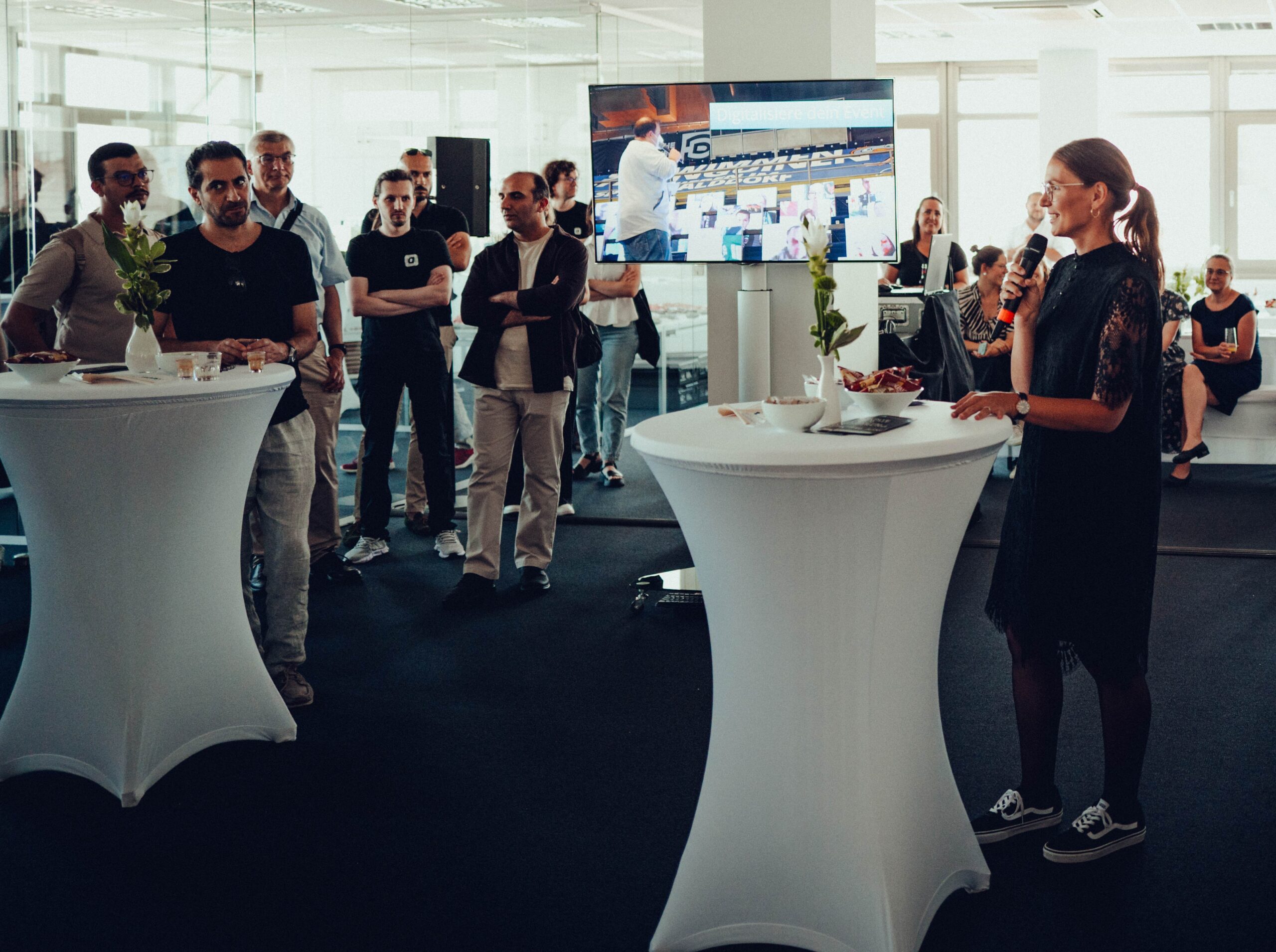 A speaker with a microphone addresses the audience at a standing table during the “Colorful Night of Digitalization.”